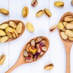 top-view-pistachio-nuts-wooden-spoons-white-background